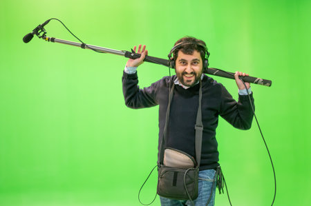 Boom microphone operator testing sound at TV studio on green key chroma background.の写真素材