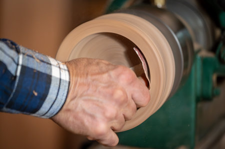 Closeup of carpenter sanding wooden product using sandpaper on a lathe.の写真素材