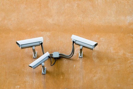 Three surveillance cameras on terracotta wallの写真素材