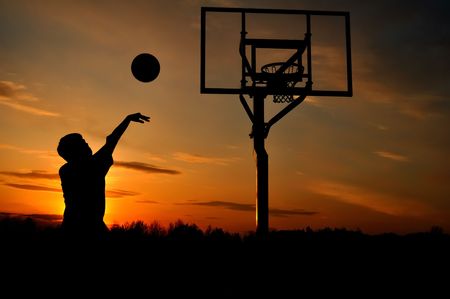 Silhouette of a Teen Boy Shooting a Basketball at Sunset, copy spaceの写真素材