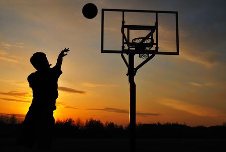 Silhouette of Teen Boy Shooting a Basketball at Sunsetの写真素材