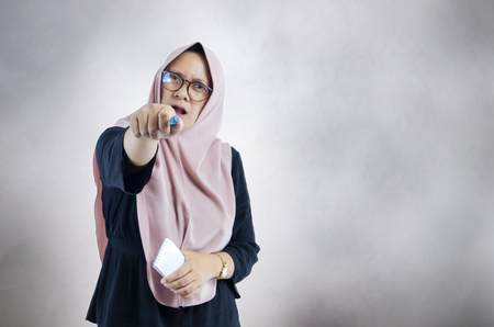 Muslim woman pointing at you using her pens, with hijab or head scarfの写真素材