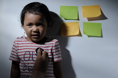 Sick little girl being observed by doctor with a stethoscope health and medical concept, blank post notes besides herの写真素材
