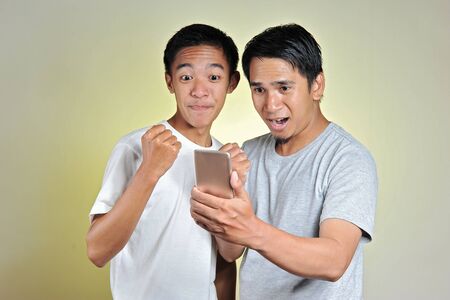 Portrait two young Asian men surprised, two young Asian men looking at cellphones screen. Amazed...