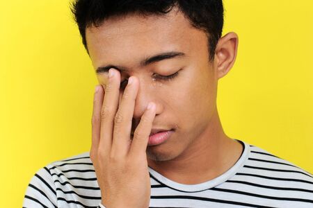 Young Asian man cry, isolated on yellow background