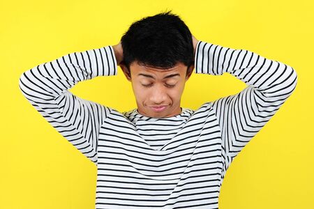 Portrait of funny Asian man showing a sleepy gesture. feeling being tired from hard work, isolated on yellow backgroundの写真素材