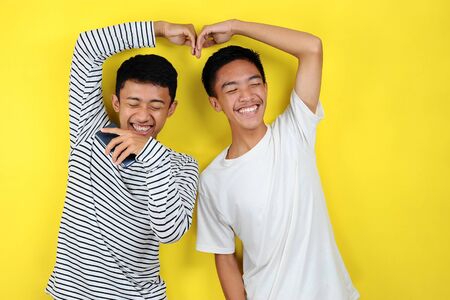 Portrait of  funny young Asian men doing crazy lovely gesture, isolated on yellow backgroundの写真素材
