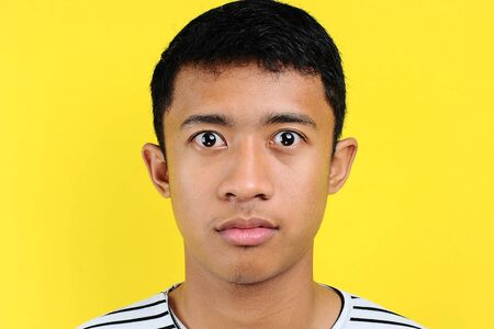 Very serious young Asian man looking at camera. On yellow backgroundの写真素材