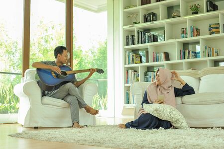 Muslim young Asian couple playing acoustic guitar together in living room. Love and romance people...