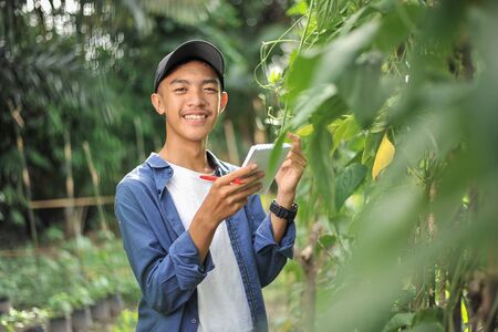 Portrait of smiling young Asian farmer man checking quality with small notebook. Happy young Asian...