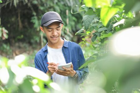 Portrait of smiling young Asian farmer man writing on the small notebook. Happy young Asian farmer...