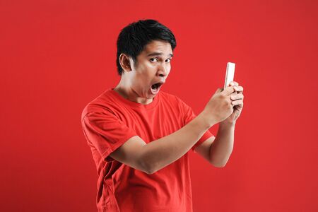 Happy Asian man reading new text on mobile, isolated on red background