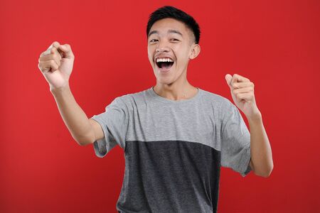 Young Asian teenager doing winning gesture, Happy get special gift, isolated on red backgroundの写真素材