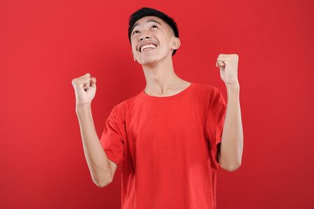Young Asian teenager doing winning gesture, Happy get special gift, isolated on red backgroundの写真素材