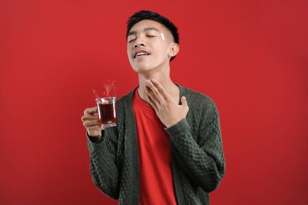 Sick cold and headache, Happy of Young Asian man wearing a sweater while drinking hot tea, isolated...