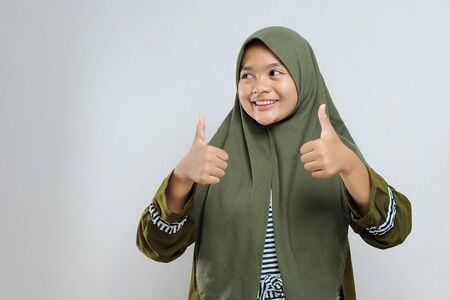 Young beautiful girl wearing muslim hijab approving doing positive gesture with hand, thumbs up...