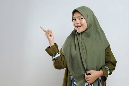 Cute Young Beautiful Muslim woman pointing copy space. Cheerful muslim woman pointing at copy space on gray background.の写真素材