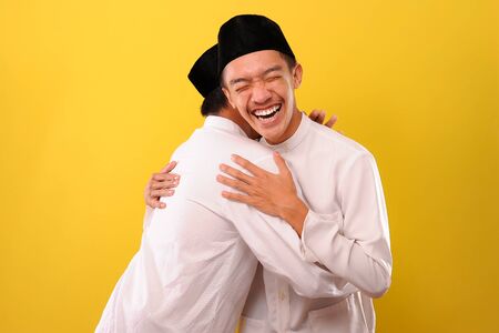 Image of happy two Young Asian Muslim men hugging each other during Eid Mubarak celebration on 1441 H, over yellow backgroundの写真素材