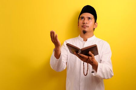 Portrait Young Asian Muslim man pray to Allah with holding the Quran and prayer beads peacefully,...