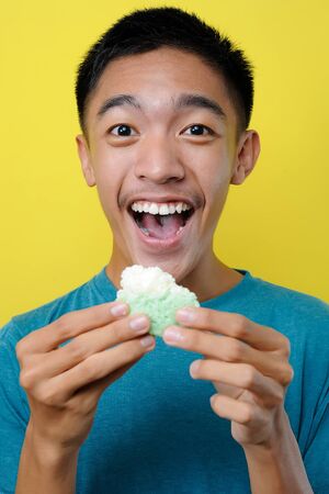 Happy Excited Young Asian man eating cake, isolated on yellow backgroundの写真素材