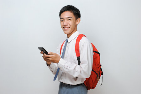 Senior High School Student of Indonesia with uniform holding mobile phone smiling looking at the...