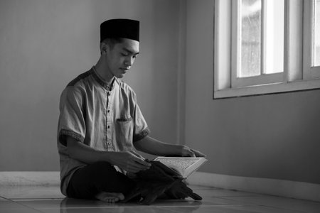 Portrait black and white image of Young Asian Muslim man reading holy Qur'an on Ramadan Kareem at...