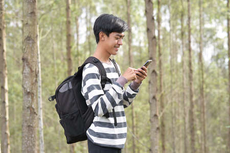 Modern Asian guy holding mobile phone in nature. Travel, technology and healthy lifestyle concept.