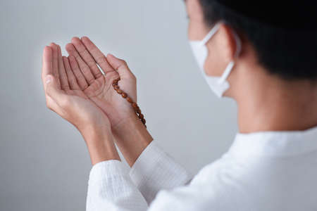 Close up Hand holding a muslim beads or tasbih with on grey background, pray to God in pandemic...