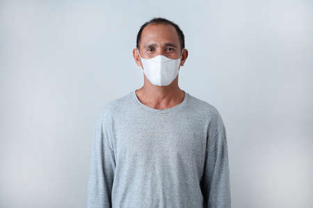 Asian Senior Man standing wearing a face mask in casual t-shirt against on grey backgroundの写真素材