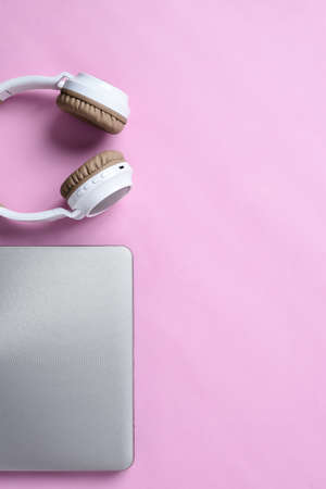 Top View Flatlay of modern wireless headphone and minimalist laptop on pink color workspace