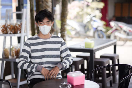 Young Asian man wears face mask to protect virus, sitting at the cafeの写真素材