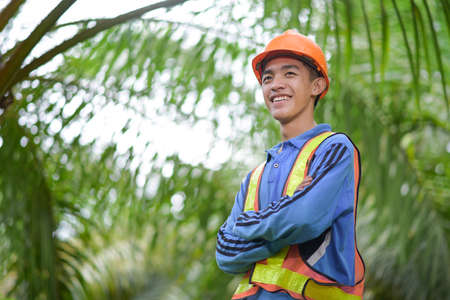Portrait of Asian palm oil  farmer with a safety helmet and work vest at palm oil plantation
