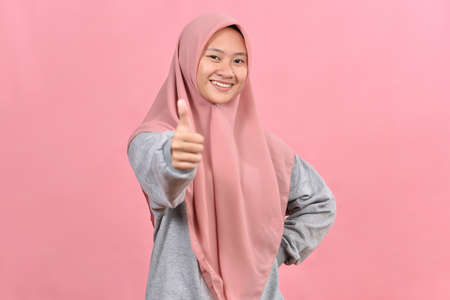 Young Asian Muslim woman showing thumb up against pink colour background. Mock up copy space. Showing thumb up.の写真素材