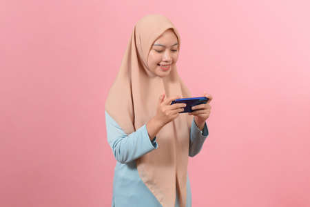 Happy Asian portrait beautiful cute young woman teen smiling typing text message on smart mobile phone enjoys online communication isolated on pink backgroundの写真素材