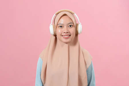 Portrait of smiling Young Asian muslim female wearing headphone against over pink backgroundの写真素材