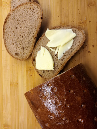 Rustic rye bread with butter on a cutting board in the kitchen