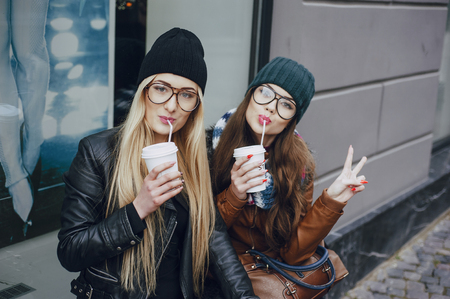 two beautiful girls walk around town fashionably and stylishly dressed with a Cup of coffeeの写真素材