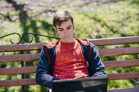 Man on computer, tablet and phone sitting on a bench on a sunny day and walk in the parkの写真素材
