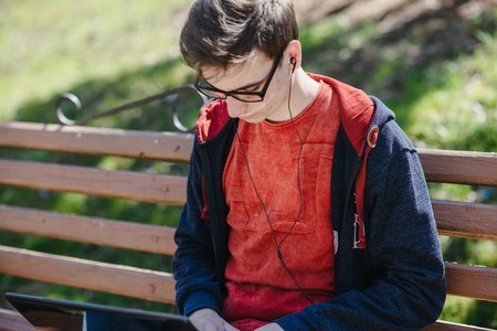 Man on computer, tablet and phone sitting on a bench on a sunny day and walk in the park