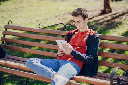 Man on computer, tablet and phone sitting on a bench on a sunny day and walk in the parkの写真素材