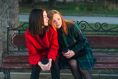Girls walking around town on a sunny day with phones sitting on a bench and drink coffeeの写真素材