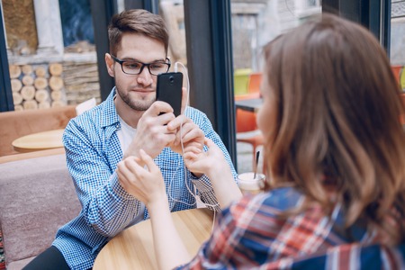 The boy and girl resting in cafe, photographed on the phone and listening to music on headphones
