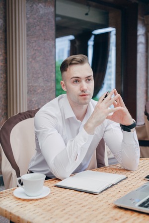 young businessman walks through the city, drinking coffee in a cafe and engaged in work