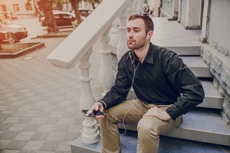 A guy in a nice town, walking, listening to music and taking pictures themselves on the phoneの写真素材