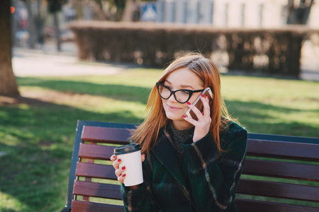 Girls walking around town on a sunny day with phones sitting on a bench and drink coffeeの写真素材
