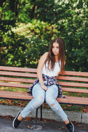 young girl sitting on a bench in the park.の写真素材
