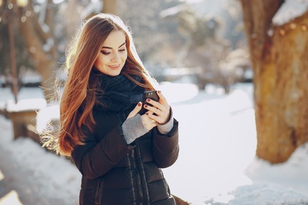 girl walking on snow-covered town, drinking coffee, photographed on the phone and riding on a sledの写真素材