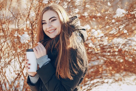 girl walking on snow-covered town, drinking coffee, photographed on the phone and riding on a sled