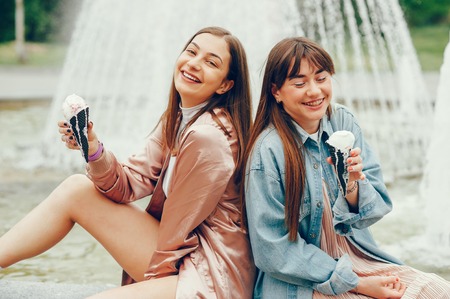 Two girls sitting near the fountain and going ice cream.の写真素材