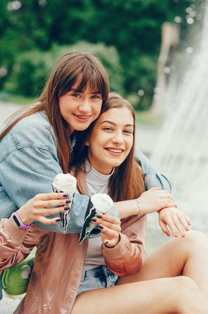 Two girls sitting near the fountain and going ice cream.の写真素材